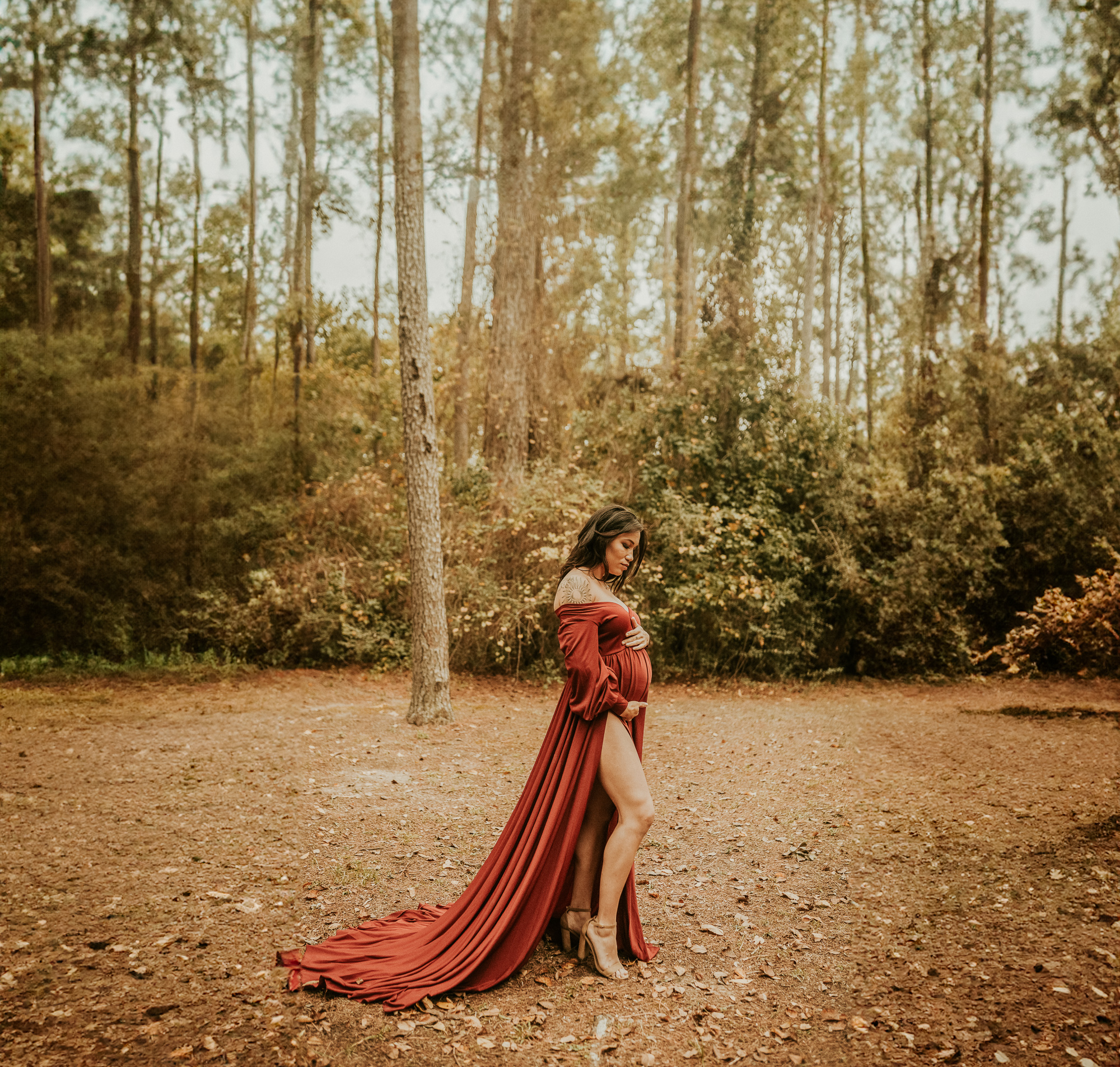 Pregnant woman posing in a forest with a flowing maroon dress in Houston, Texas. Photography taken by Helena Photographs